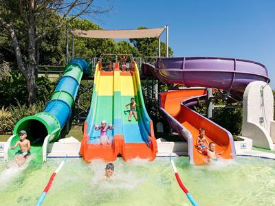 Bunte Wasserrutschen münden in ein Becken, Kinder rutschen bei sonnigem Wetter hinunter.