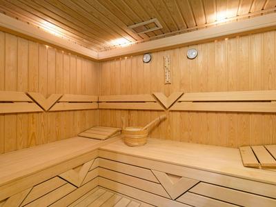 Helle Holzsauna mit Eckbänken, Holzeimer und Schöpflöffel, beleuchtet von Deckenlampen.