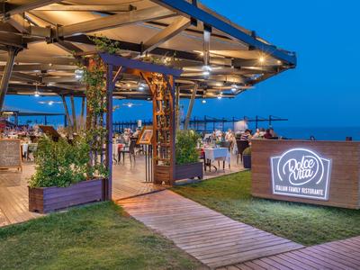 Offenes Restaurant mit Holzweg, moderner Beleuchtung und Blick auf das Meer bei Abenddämmerung.