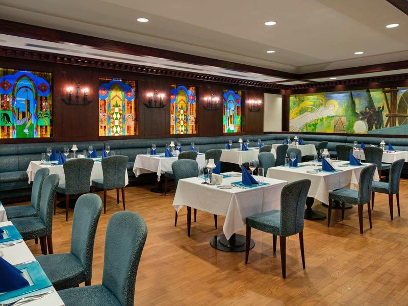 Salle à manger moderne avec tables dressées et fresques murales colorées.