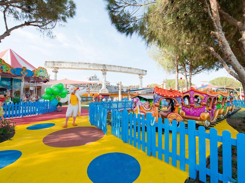 Parc d'attractions coloré avec carrousel, clôture bleue et arbres en arrière-plan.