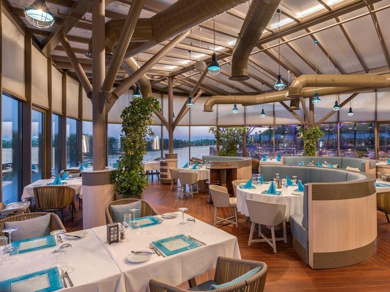 Restaurant moderne avec poutres en bois et grandes fenêtres donnant sur une ville la nuit.