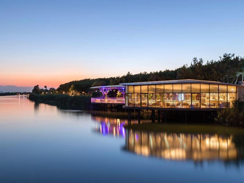 Bâtiment moderne avec grandes fenêtres au bord d'une eau calme au coucher du soleil