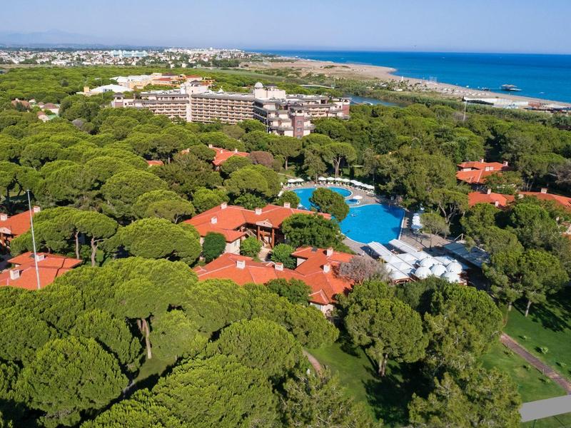 Vue aérienne d'un complexe avec piscine, entouré d'arbres verts et près de la mer.