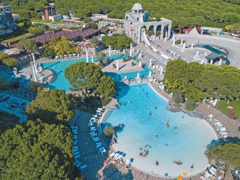 Grand complexe avec plusieurs piscines, chaises longues et environnement verdoyant.