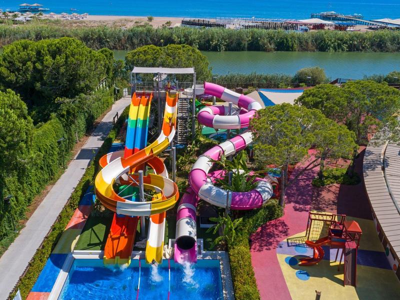 Toboggans aquatiques colorés près de la piscine et de la verdure dans une station avec vue sur le lac et la mer.