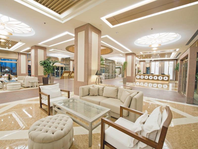 Hall d'hôtel lumineux avec coins salons modernes, luminaires décoratifs au plafond et sol poli.