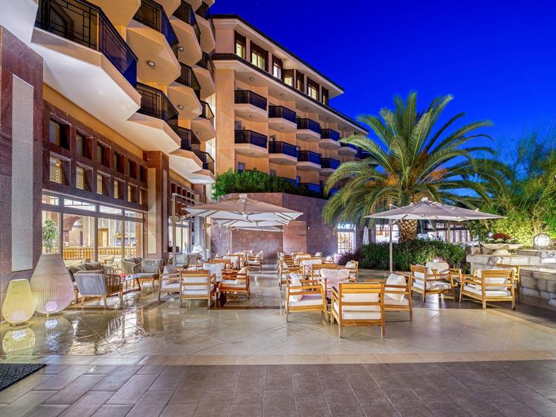 Espace extérieur d'un hôtel avec sièges confortables, palmiers et ambiance détendue en soirée.