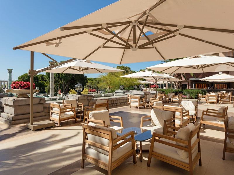 Terrasse ensoleillée d'hôtel avec mobilier en bois et grands parasols donnant sur la côte.