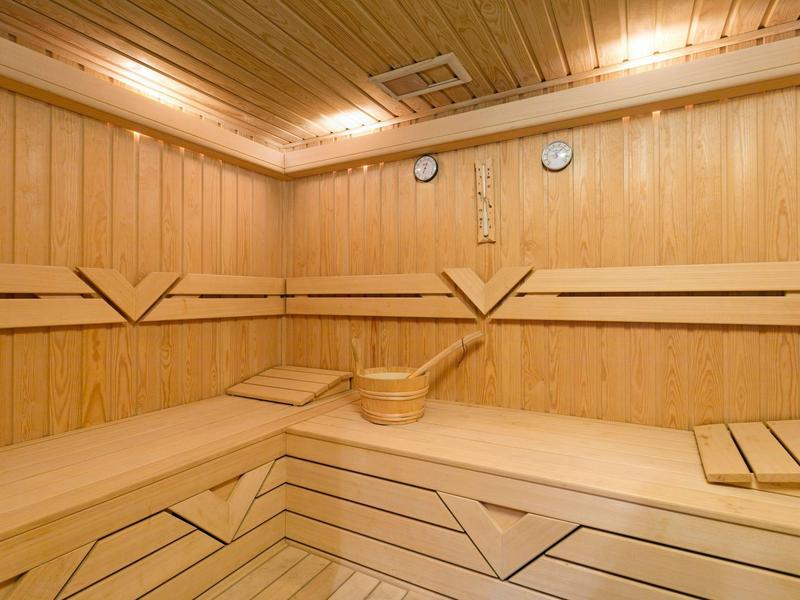 Sauna lumineuse en bois avec des sièges à niveaux et un seau en bois.