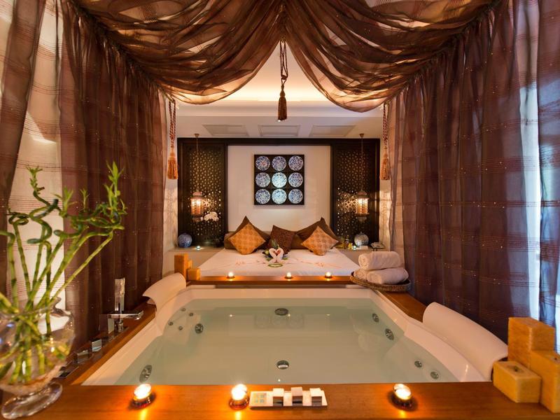 Bain spa luxueux avec bougies, coussins et rideaux créant une ambiance relaxante.