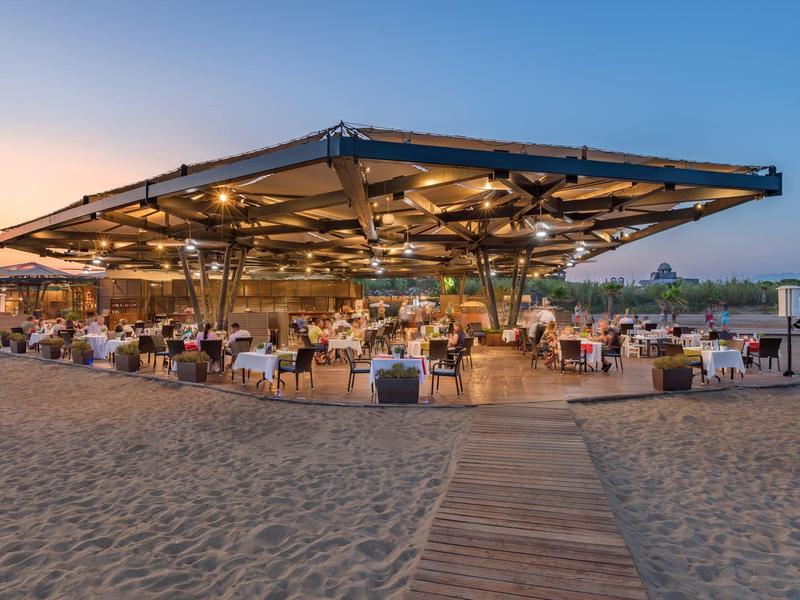 Restaurant de plage moderne avec espaces assis couverts et vue sur la mer au coucher du soleil.