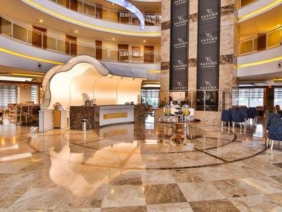 Prostorná hotelová lobby s mramorovými podlahami, výtahy a posezením v elegantním kulatém prostoru.