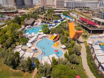 Widok z lotu ptaka na duży kompleks hotelowy z basenem, zjeżdżalniami wodnymi i słonecznymi miejscami do leżenia.
