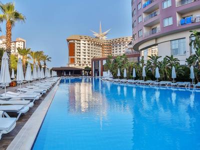 Basen hotelowy z leżakami, parasolami i nowoczesną architekturą hotelu w tle.