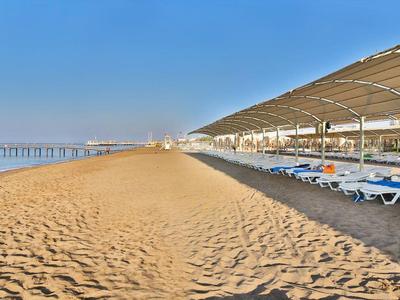 Prázdná pláž s lehátky a slunečníky pod modrou oblohou, klidná a lákavá.