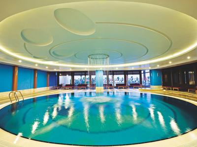 Okrągły kryty basen z eleganckim sufitem i dużymi oknami wpuszczającymi naturalne światło.