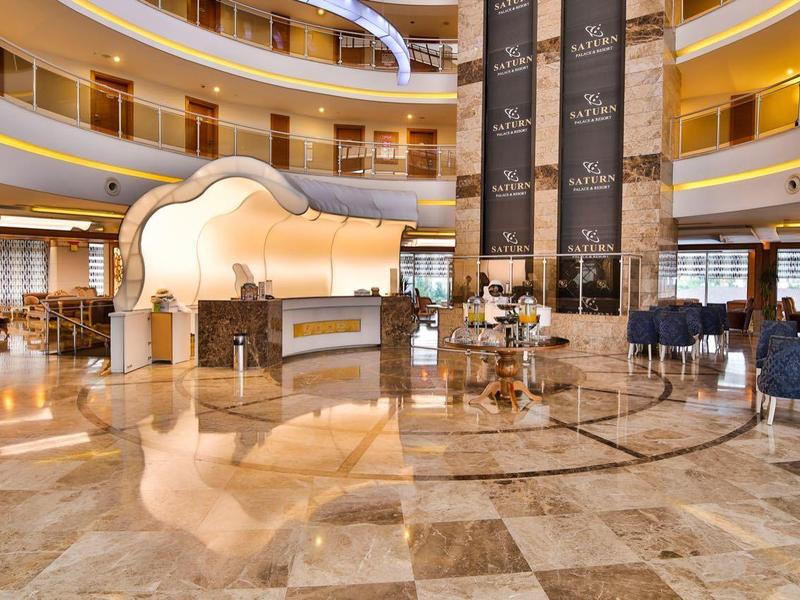 Prostorná hotelová lobby s mramorovými podlahami, výtahy a posezením v elegantním kulatém prostoru.