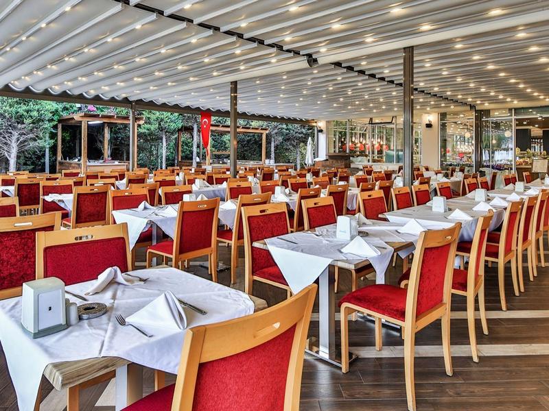 Velká krytá jídelna s stolky, bílými ubrusy a červenými židlemi v hotelu.