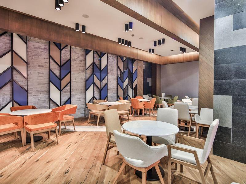Moderní hotelová lounge s dřevěnou podlahou, bílými a oranžovými židlemi a dekorativní stěnou.