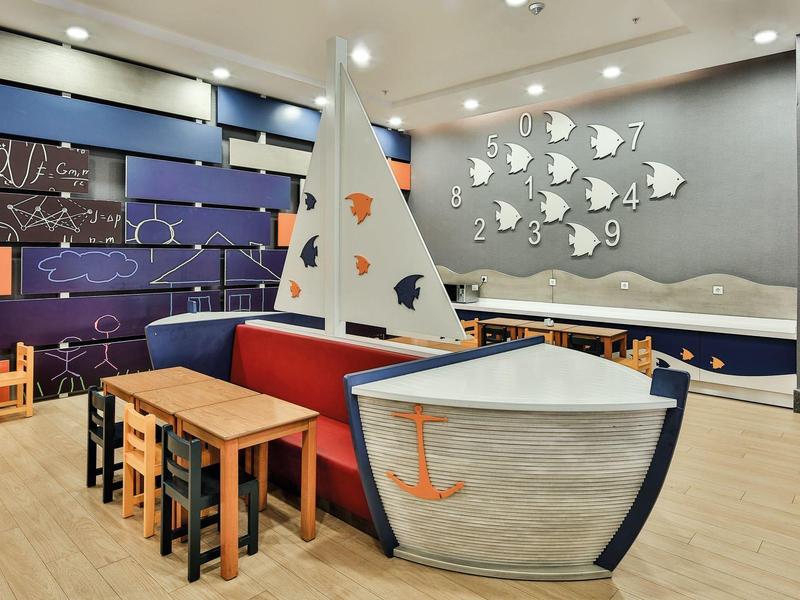 Dětský koutek s lodním tématem a barevnými stoly v hotelovém interiéru.