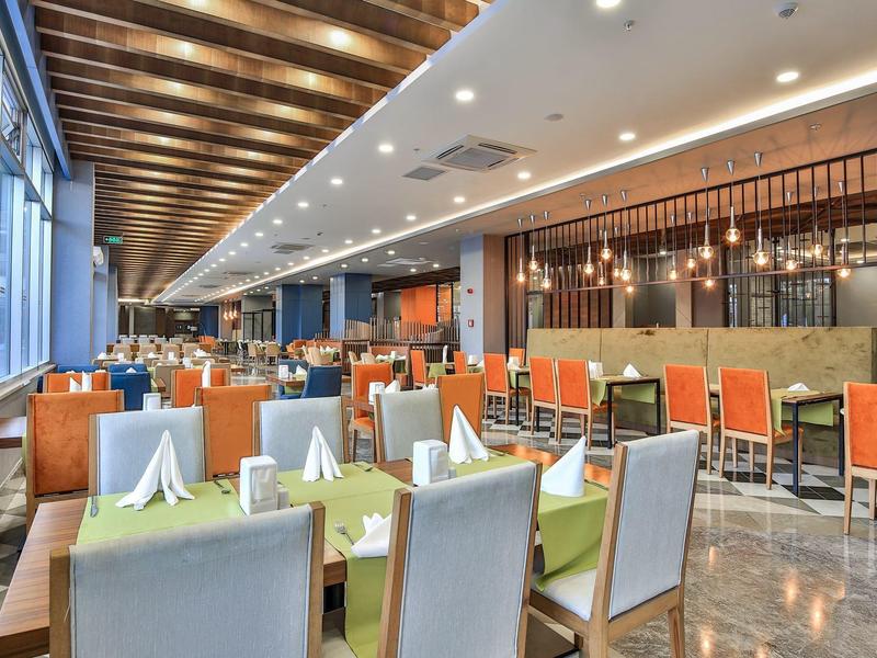 Moderní interiér hotelové restaurace se prostřenými stoly a oranžovými židlemi pod dřevěným stropem.