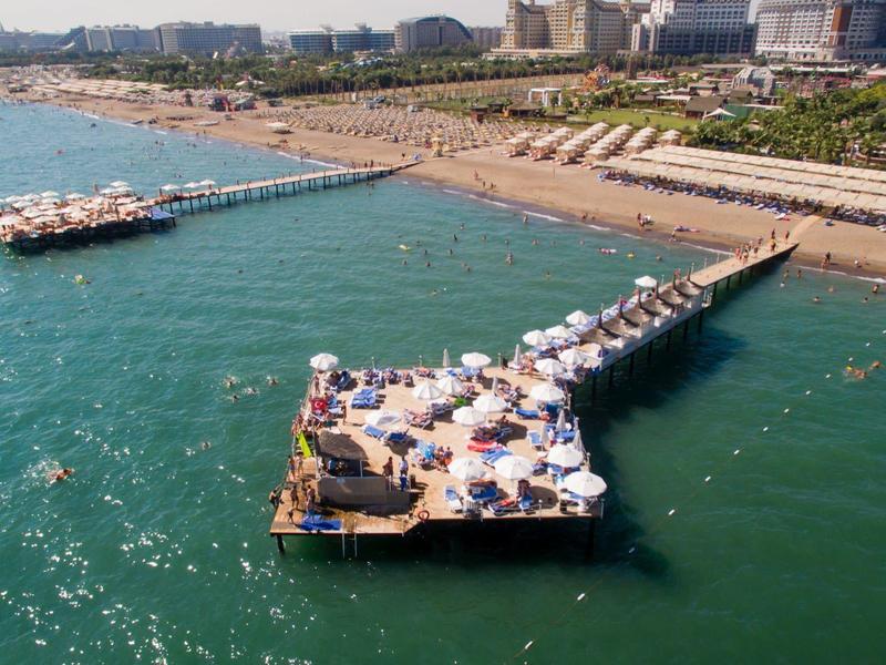 Dlouhé dřevěné molo s slunečníky a lehátky u přímořské pláže s modrým mořem