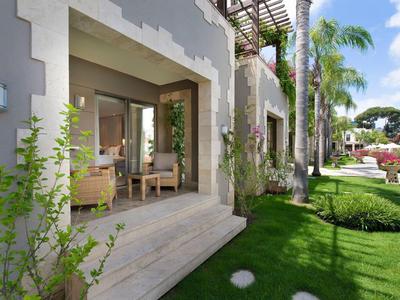 Terrazze dell'hotel con porte aperte, area salotto e giardino verde con prato e palme.