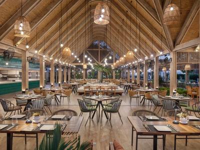 Grand restaurant ouvert avec toit en bois et lumières modernes dans un complexe hôtelier.