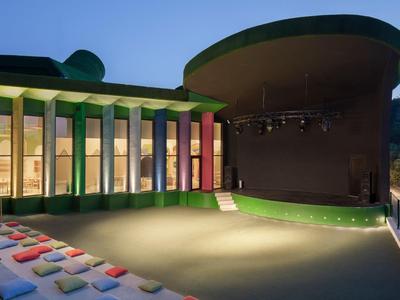 Vista serale di un teatro all'aperto moderno con cuscini colorati e area del palco illuminata.