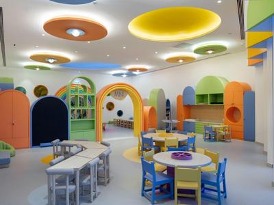 Sala giochi colorata per bambini con tavoli, sedie e archi rotondi dai colori vivaci.
