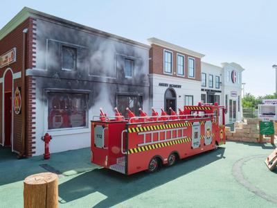 Replica di una casa in fiamme con camion dei pompieri in un parco divertimenti.