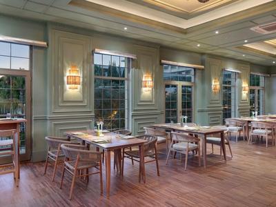 Area ristorante dell'hotel luminosa con tavoli in legno e grandi finestre che si affacciano sulla natura.