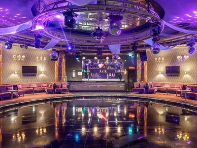 Boîte de nuit moderne avec éclairage coloré, bar et sièges rembourrés en demi-cercle.