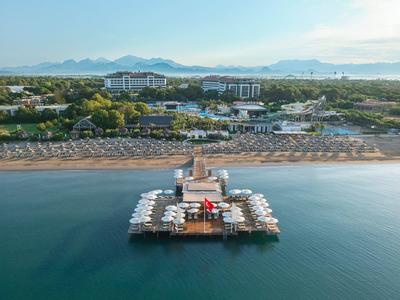 Vista aerea di un molo con molte ombrelloni su una spiaggia tranquilla davanti a un complesso alberghiero.