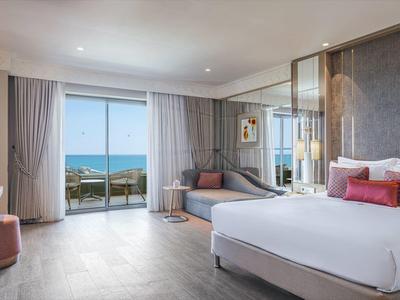 Camera d'hotel moderna con letto grande, divano, balcone e vista mare.