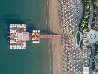 Veduta aerea di un resort sulla spiaggia con molo, ombrelloni e lettini sulla sabbia.