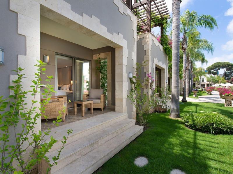 Terrazze dell'hotel con porte aperte, area salotto e giardino verde con prato e palme.