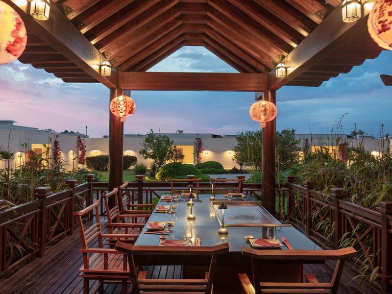 Accogliente terrazza di ristorante con tavolo e sedie in legno sotto luci di lanterne al crepuscolo.