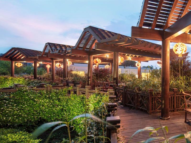 Area esterna serale con pergolati in legno illuminati e aree salotto tra il verde.