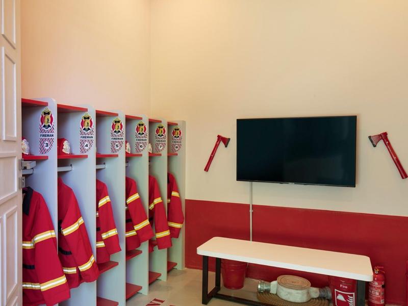 Caschi e uniformi antincendio in spogliatoio con TV montata a parete