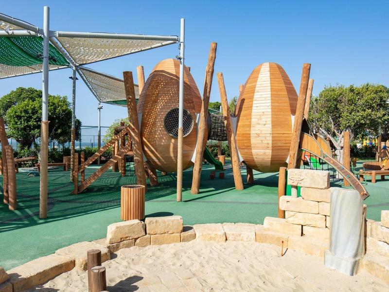 Area gioco moderna con strutture in legno e zona sabbiosa sotto un cielo limpido