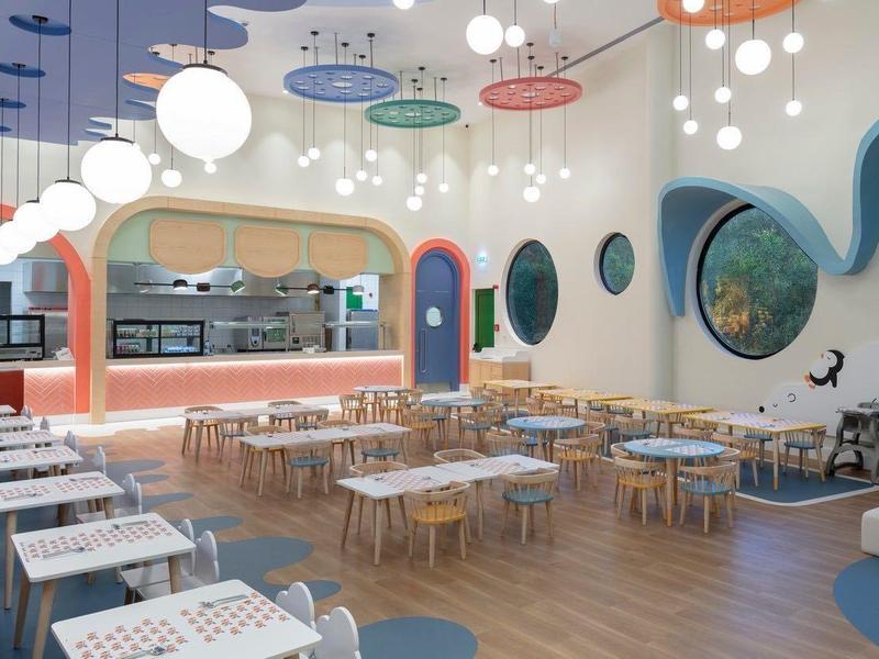 Ristorante d'hotel moderno con finestre rotonde colorate, luci circolari e pavimento in legno.