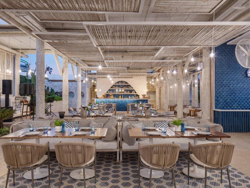 Ristorante moderno con soffitto in legno, pavimento decorato e vista aperta sul mare.