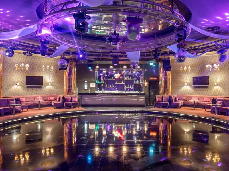 Grande discoteca moderna con palco, illuminazione colorata e pista da ballo in ambiente alberghiero.