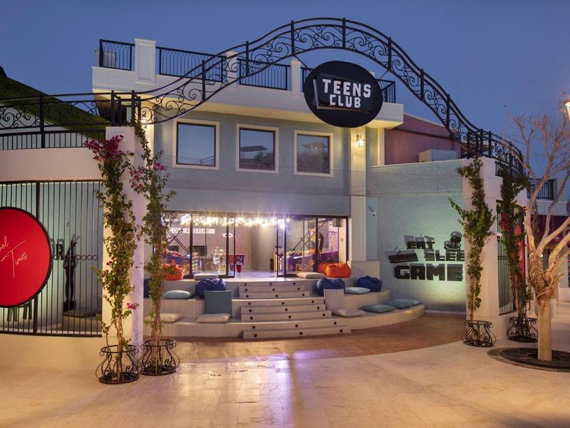 Ingresso di un Teens Club con illuminazione moderna e aree salotto al crepuscolo.