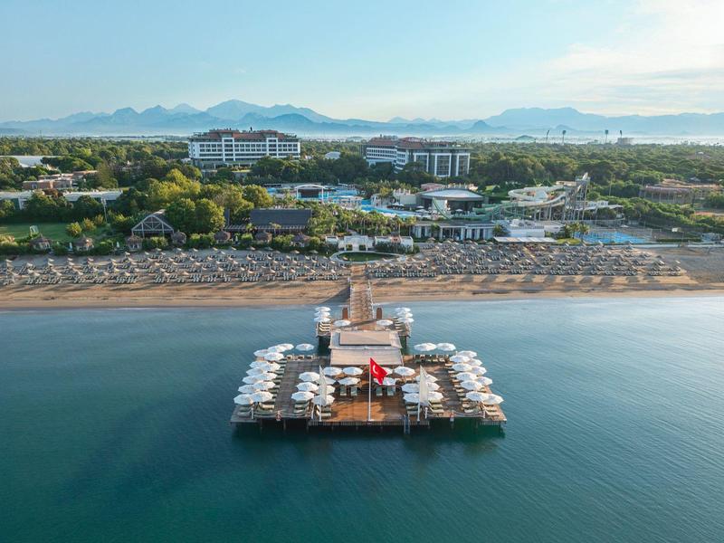 Vista aerea di un molo con molte ombrelloni su una spiaggia tranquilla davanti a un complesso alberghiero.