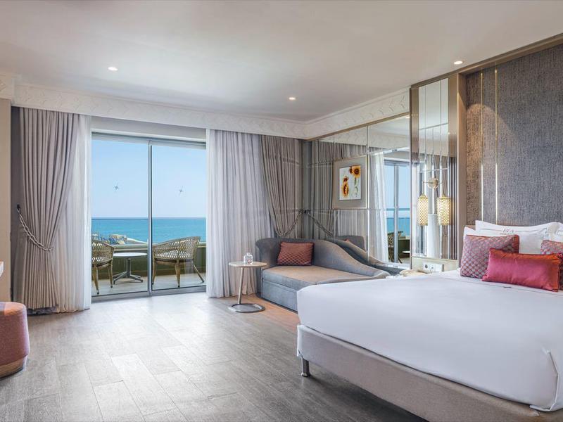 Camera d'hotel moderna con letto grande, divano, balcone e vista mare.