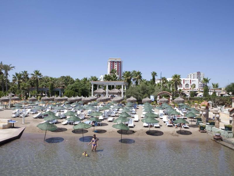 Pláž u bazénu s lehátky a slunečníky pod jasnou oblohou.