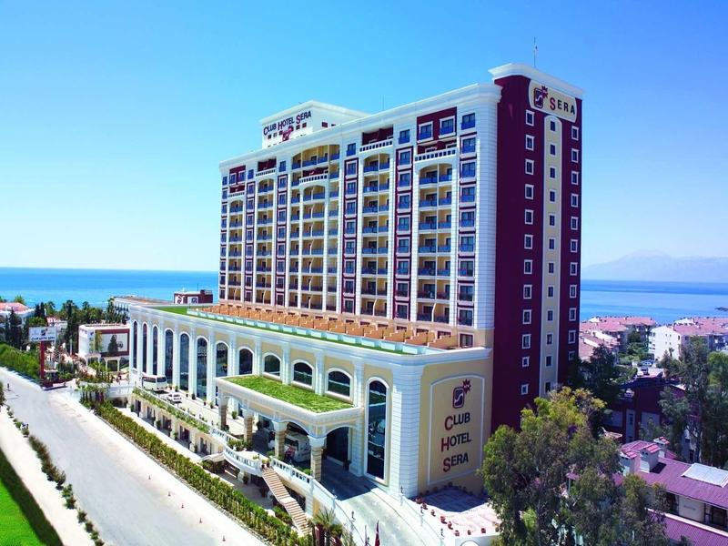 Velký moderní hotel u moře s balkony a okolní zelení.